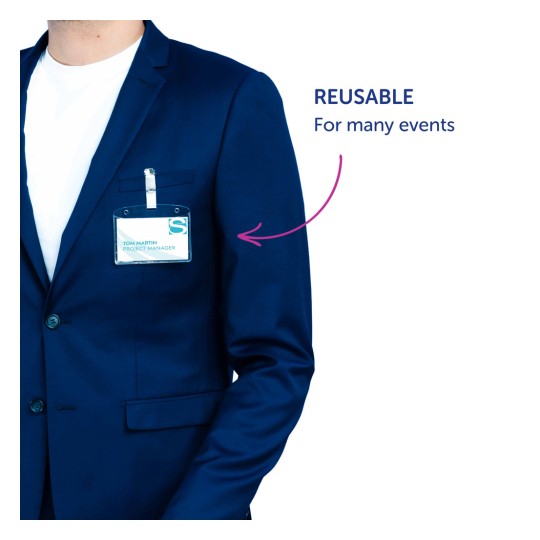 Bildet viser en person iført en marineblå blazer med en synlig navnelapp på brystet. Navnelappen viser navnet 'Tom Martin' og tittelen 'Prosjektleder'. En merknad peker på lappen og sier 'GJENBRUKBAR For mange arrangementer'.