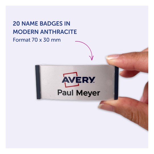 Bildet viser en hånd som holder et navneskilt merket 'Avery' med navnet 'Paul Meyer', og indikerer at det er en del av et sett med 20 skilt i moderne antrasittfarge, som måler 70 x 30 mm.