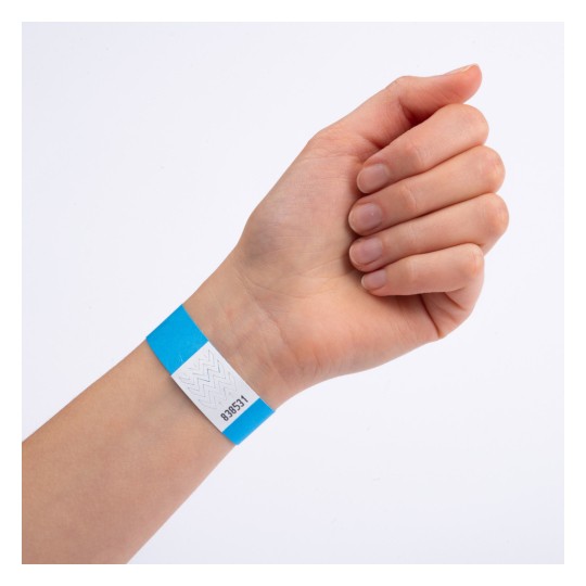 Bildet viser en hånd som har på seg et blått og hvitt armbånd. Armbåndet har en kode trykket på seg, som muligens indikerer adgang eller inngang til et arrangement.