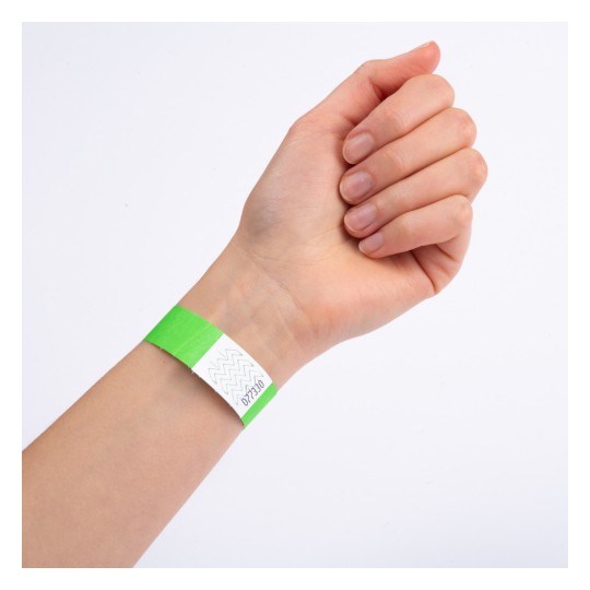 Et nærbilde av en hånd med et grønt armbånd på håndleddet. Armbåndet har en hvit del med et sikksakkmønster og ser ut til å være merket med et nummer.