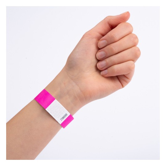 Bildet viser en hånd med et rosa armbånd som har en hvit etikett og et nummer trykt på. Hånden er posisjonert med fingrene lukket, og armbåndet er tydelig synlig.