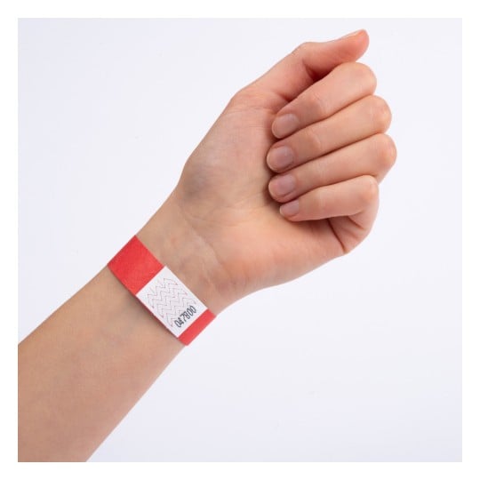 En hånd med et rødt armbånd med en hvit etikett som har sikksakkmønstre og tall trykt på.