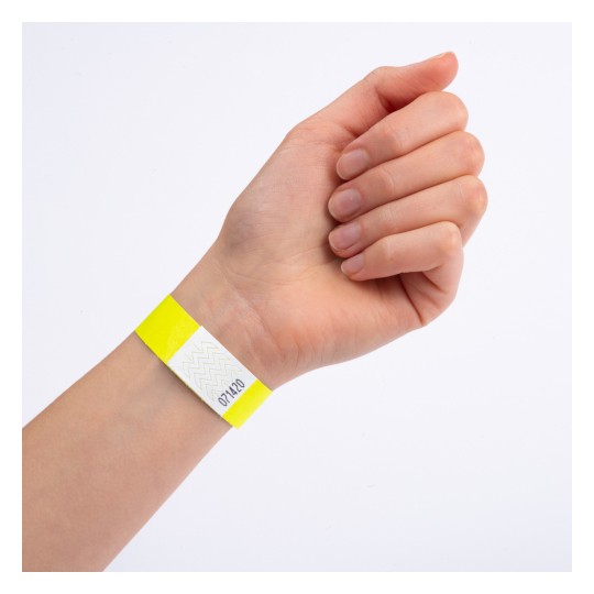 Dette bildet viser en hånd med et gult armbånd som har en hvit seksjon med et sikksakkmønster og et nummer på.