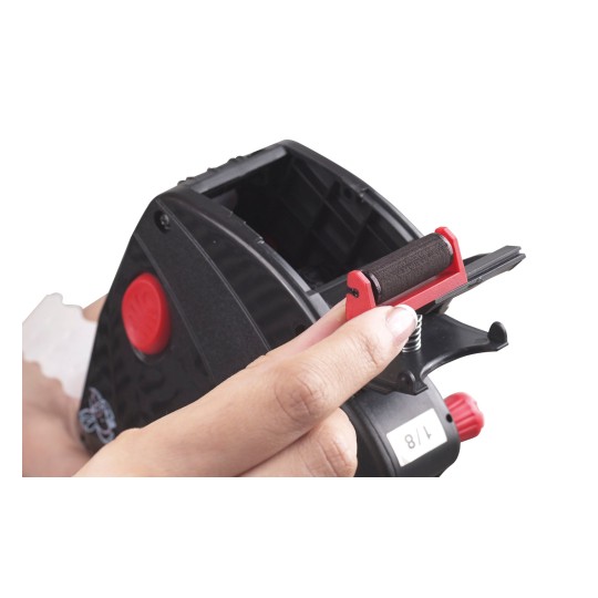 Bildet viser en hånd som holder et svart og rødt verktøy med en rull. Det ser ut til å være en limdispenser eller en merkemaskin, med en synlig rød knapp og et merkingshjul for å endre teksten.