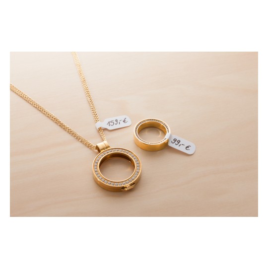 Bildet viser et gullkjede og en gullring plassert på en treoverflate. Kjedet har et sirkulært anheng dekorert med glitrende steiner, og begge gjenstandene har prislapper: €159 for kjedet og €99 for ringen.