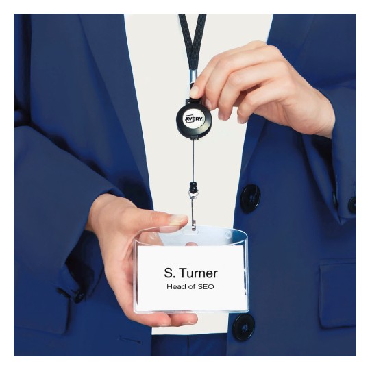 En person iført en blå dress holder et uttrekkbart navneskilt. Skiltet viser navnet 'S. Turner' og tittelen 'Leder for SEO'.