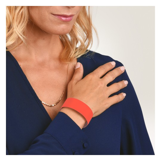 Bildet viser en kvinne med blondt hår som har på seg en mørk blå bluse, med en hånd plassert på skulderen. Hun har et tynt halskjede og bærer et oransje armbånd på håndleddet.