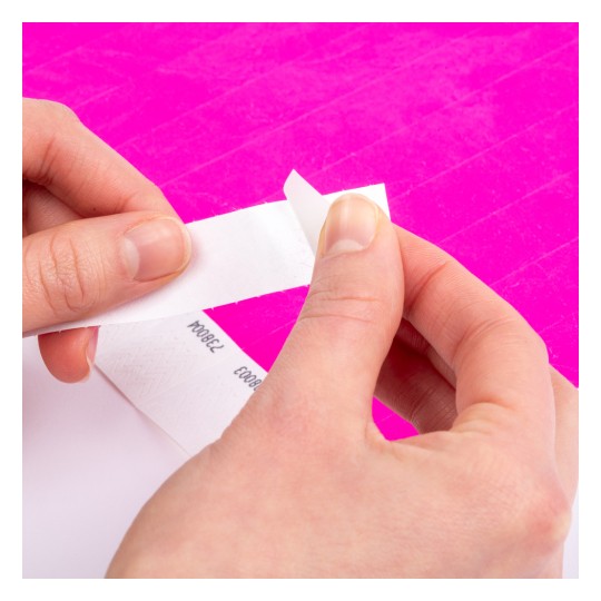 En persons hender holder en stripe med hvit tape, med en synlig lys rosa bakgrunn. Tapen ser ut til å ha noen markeringer på seg.