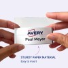 Bildet viser en person som holder en navnelapp med navnet 'Paul Meyer' og en Avery-logo, noe som indikerer at den er laget av robust papirmateriale og er enkel å sette inn.