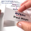 Bildet viser en hånd som holder et navneskilt hvor det står 'Avery Paul Meyer.' Det fremhever hvor lett det er å løsne skiltet, med vekt på glatte kanter.
