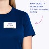 Bildet viser en person som har på seg en marineblå skjorte med et navneskilt som sier 'Avery B. Carlos, Markedsføringsdirektør'. Det er en tekstetikett ved siden av personen som indikerer 'Høy Kvalitet Tekstilfilm' og nevner at den har en myk følelse som passer tett til klær.