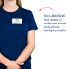 Bildet viser en person med en marineblå skjorte og et navneskilt som viser 'B. Carlos, Markedsføringsdirektør.' I tillegg er det tekst som beskriver navneskiltets selvklebende egenskap, som sier at det fester seg pålitelig til klær og fjernes enkelt uten å etterlate rester.