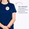 Bildet viser en person som har på seg en blå t-skjorte med en selvklebende navnelapp som lyder "B. Carlos, Markedsføringsdirektør." Teksten fremhever at lappen fester seg pålitelig til klær og kan fjernes enkelt uten å etterlate rester.