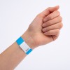 Bildet viser en hånd som har på seg et blått og hvitt armbånd. Armbåndet har en kode trykket på seg, som muligens indikerer adgang eller inngang til et arrangement.