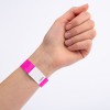 Bildet viser en hånd med et rosa armbånd som har en hvit etikett og et nummer trykt på. Hånden er posisjonert med fingrene lukket, og armbåndet er tydelig synlig.
